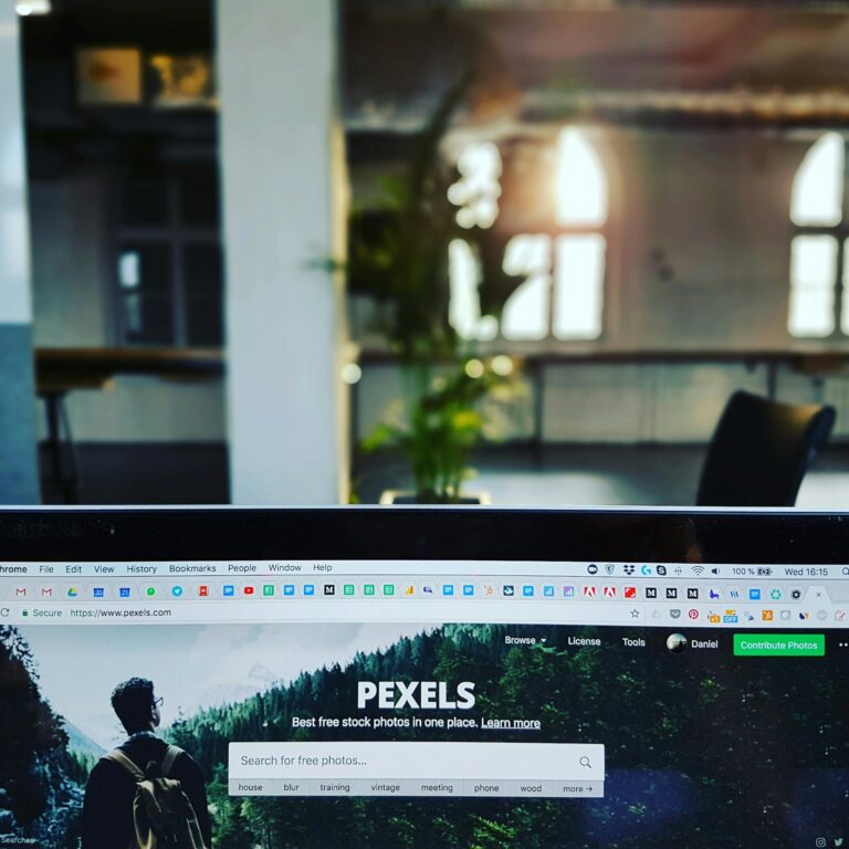 A close-up of a laptop displaying the Pexels website in a sunlit, modern office.